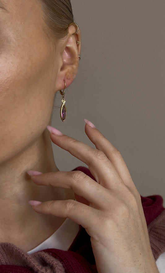 Close-up of a person wearing a gold earring with a purple gemstone on a neutral background
